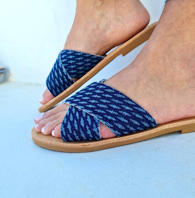 K&ouml;nnte beinhalten: Ein Paar blaue Jeans-Sandalen mit gekreuzten Riemen. Die Sandalen haben eine braune Ledersohle.