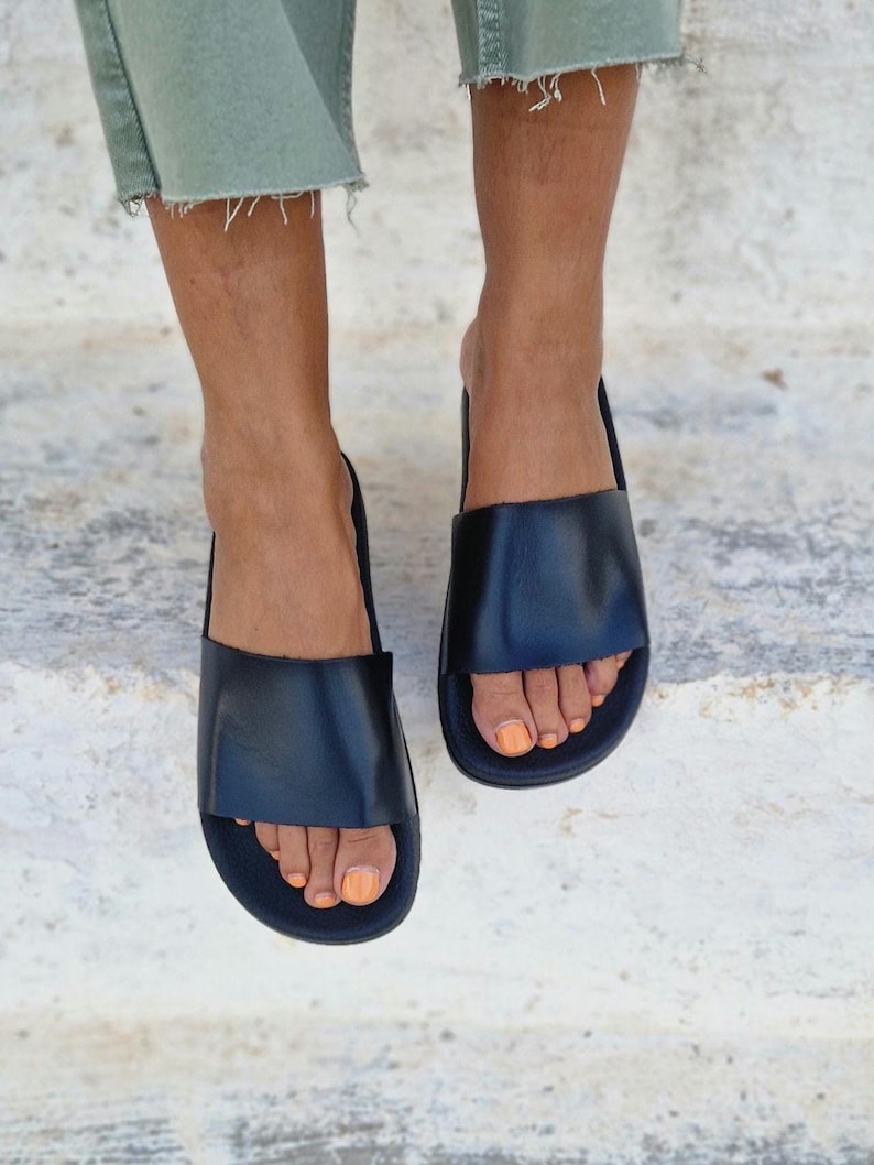 以下が含まれることがあります： シンプルなデザインの黒い革製のサンダル。フラットソールと足の甲に渡る幅広のストラップが特徴です。