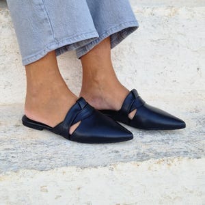 May include: Black leather pointed toe mules with a cut-out detail and a braided strap across the vamp.