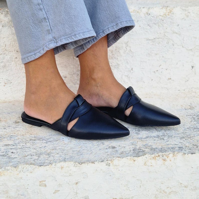 May include: Black leather pointed toe mules with a cut-out detail and a braided strap across the vamp.