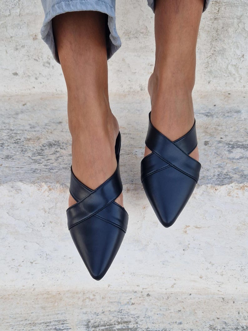 May include: Black leather pointed-toe mules with criss-cross straps.