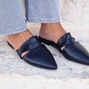 May include: A pair of black leather mules with a pointed toe and a criss-cross strap detail.