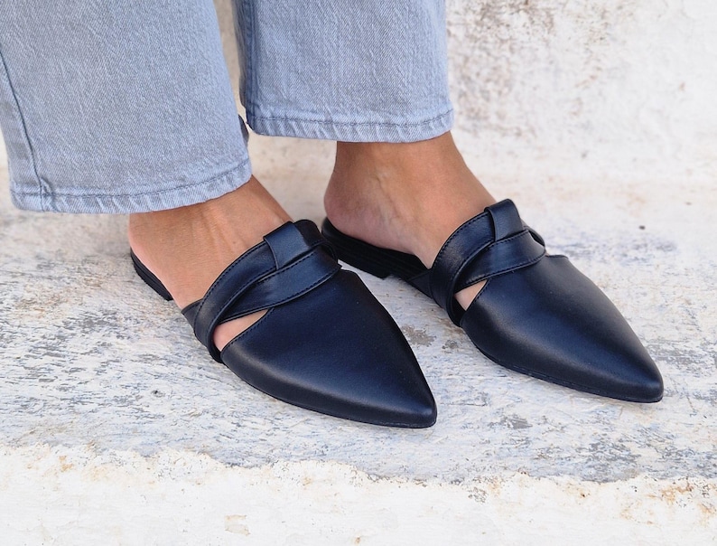 May include: A pair of black leather mules with a pointed toe and a criss-cross strap detail.