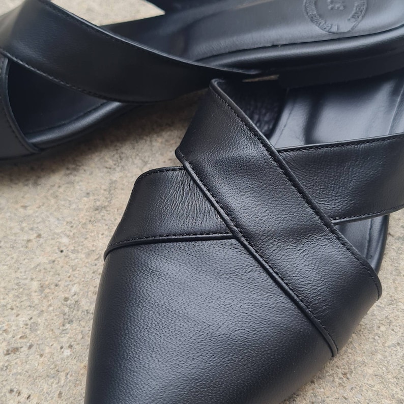 May include: A pair of black leather sandals with a criss-cross strap design. The sandals have a pointed toe and a low heel.
