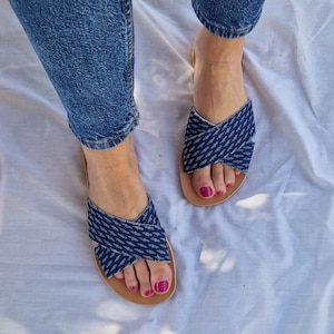 K&ouml;nnte beinhalten: Ein Paar blaue Jeans-Sandalen mit gekreuzten Riemen. Die Sandalen haben eine braune Ledersohle und werden getragen.
