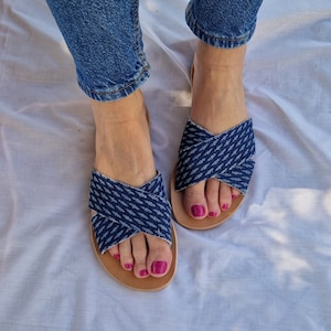 K&ouml;nnte beinhalten: Ein Paar blaue Jeans-Sandalen mit gekreuzten Riemen. Die Sandalen haben eine braune Ledersohle und werden getragen.