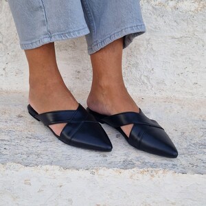 May include: A pair of black leather pointed toe mules with a criss-cross strap design.