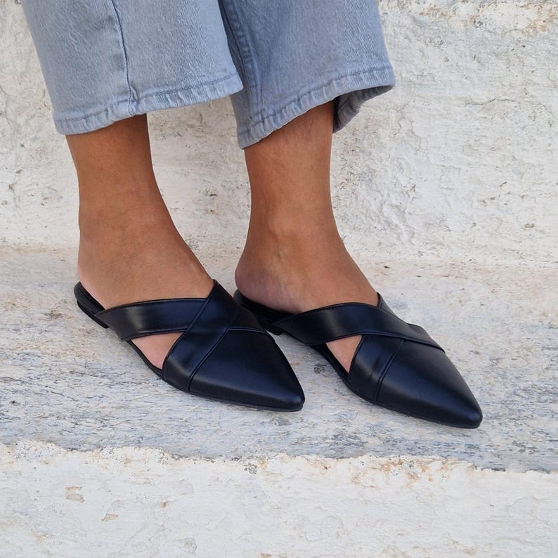 May include: A pair of black leather pointed toe mules with a criss-cross strap design.