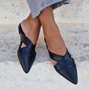 May include: A pair of black leather pointed toe mules with criss-cross straps.