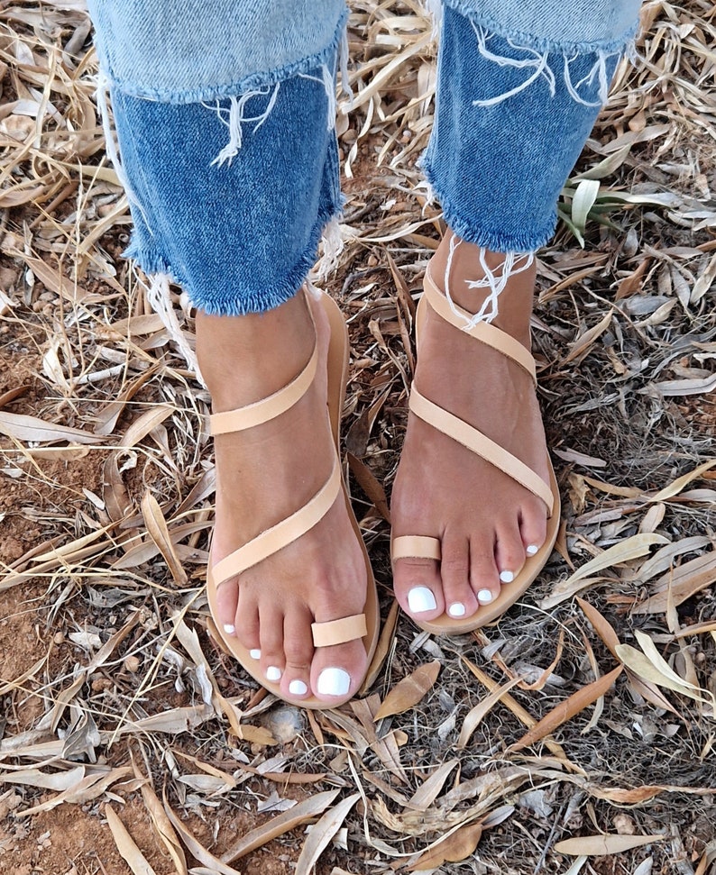 K&ouml;nnte beinhalten: Tannfarbene Ledersandalen mit mehreren Riemen, die sich um die Kn&ouml;chel und Zehen wickeln. Die Sandalen haben ein schlichtes Design und werden barfu&szlig; getragen.