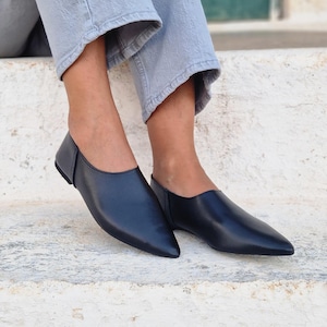 Pode incluir: Um par de sapatos baixos de bico fino em couro preto. Os sapatos s&atilde;o do tipo slip-on e t&ecirc;m um design simples e minimalista.