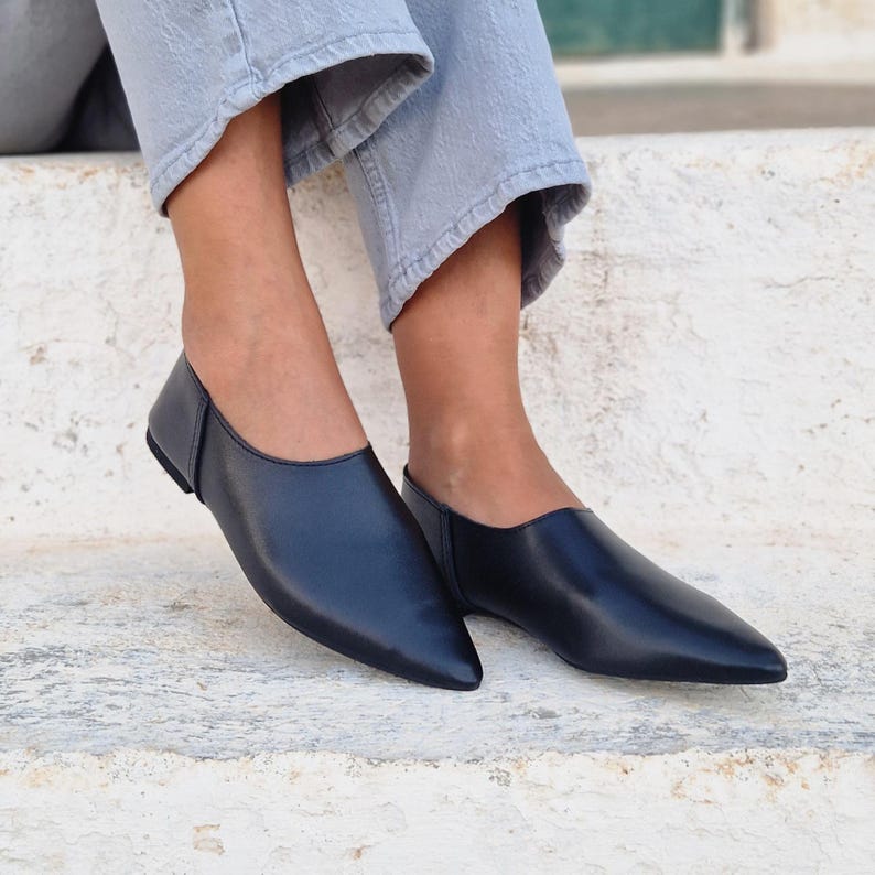 Pode incluir: Um par de sapatos baixos de bico fino em couro preto. Os sapatos s&atilde;o do tipo slip-on e t&ecirc;m um design simples e minimalista.