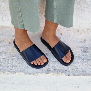 以下が含まれることがあります： 厚底の黒い革製のサンダル。足に履いています。