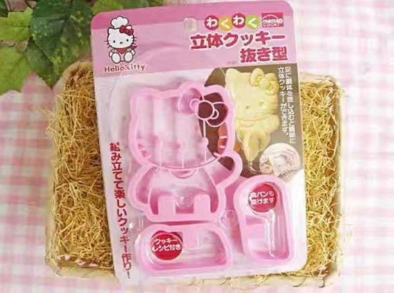 May include: Pink Hello Kitty cookie cutter set. The set includes a three-part cutter for creating 3D cookies. The packaging features Japanese text and an image of a finished cookie. The set is designed for making cookies and includes a recipe.