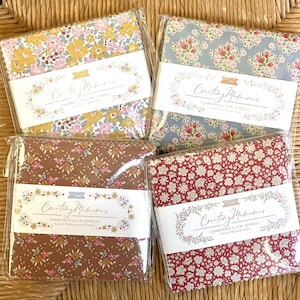 May include: Four packages of fabric charm packs, each with a different floral pattern. The packages are labeled "Creating Memories Charm Pack 5 x 5 in 32 Pieces" and feature a variety of colors, including blue, red, brown, and yellow.