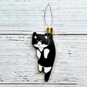 May include: Black and white cat needle threader with a gold top. The cat is facing to the left and has a white face and chest.