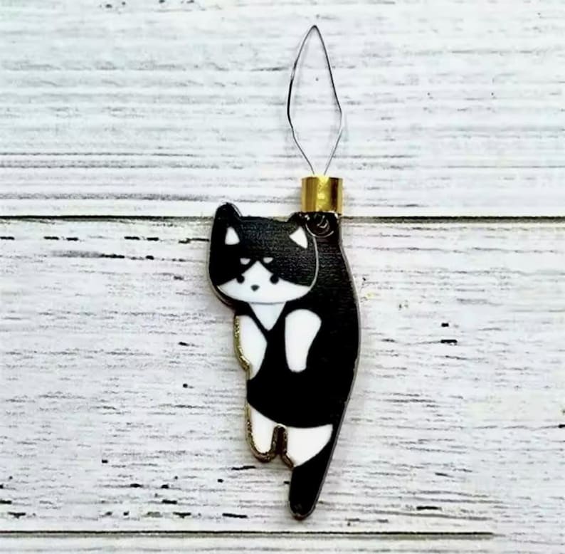 May include: Black and white cat needle threader with a gold top. The cat is facing to the left and has a white face and chest.