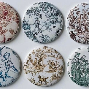 May include: Six round, white ceramic buttons with a variety of toile patterns. Each button features a different scene with people and animals in a pastoral setting. The patterns include blue, green, brown, and red.