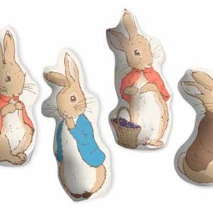 May include: Four plush rabbit-shaped pillows. Each pillow features a different illustration of a rabbit character, with details like clothing and accessories. The rabbits are in various poses, with a neutral background.