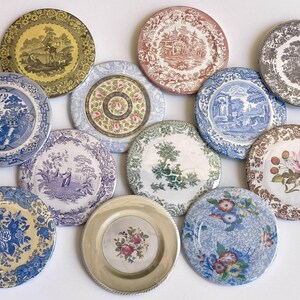May include: A collection of 11 round ceramic plates with various floral and landscape designs in shades of blue, green, brown, and pink.