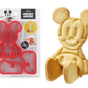 May include: A red plastic Mickey Mouse cookie cutter set next to a baked Mickey Mouse cookie. The packaging includes the Disney Mickey Mouse logo and Japanese text. The cookie cutter is designed to create a 3D cookie.
