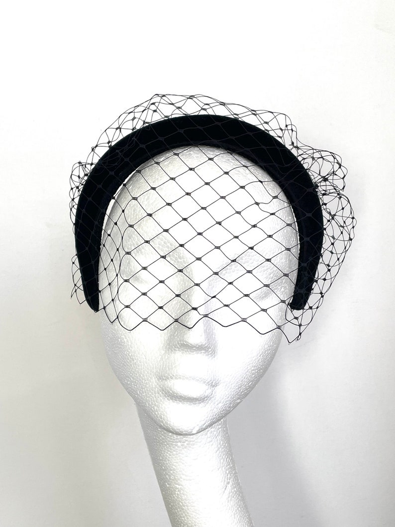 May include: A black velvet headband with a black tulle veil. The headband is wide and has a slight curve. The veil is delicate and has a diamond pattern.