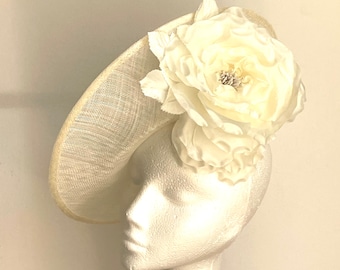 May include: A white fascinator hat with a large white flower on top. The hat is made of a delicate, woven material and has a wide brim.