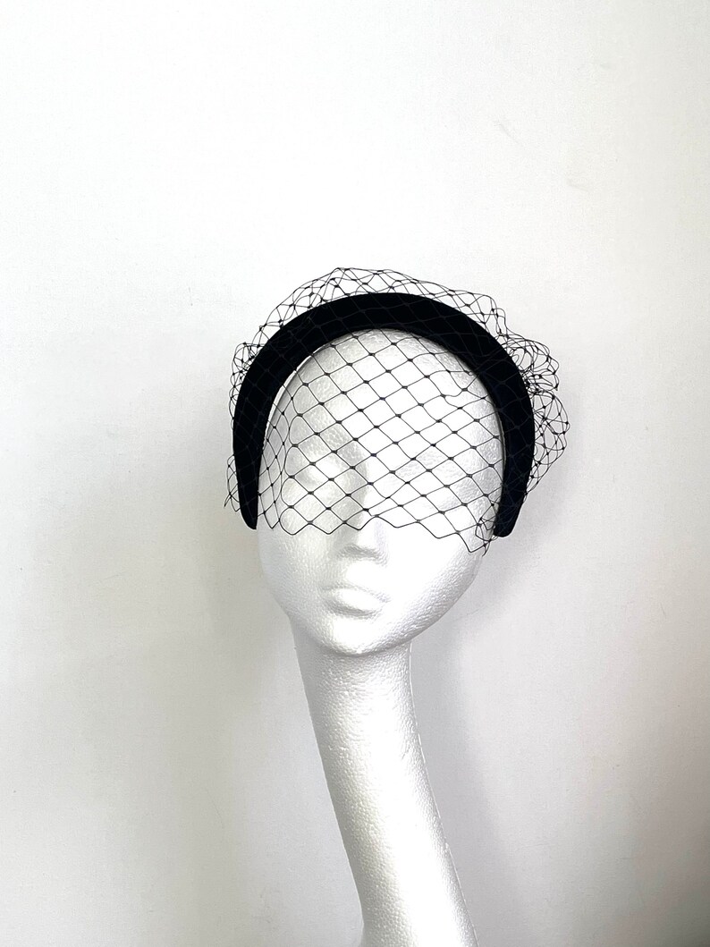 May include: Black velvet headband with a black tulle veil. The headband is curved and the veil is gathered at the top.