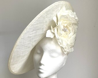 May include: A white, wide-brimmed hat with a large white flower on the side. The flower has a small rhinestone in the centre.
