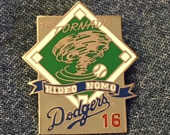 May include: A gold-colored baseball pin featuring a green baseball diamond with a tornado graphic and the text "The Tornado Hideo Nomo Dodgers 16".
