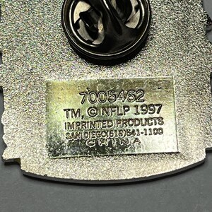 May include: A silver-toned metal pin with a black clasp. The pin has a textured background and a rectangular section with the text "7005462 TM, &copy; NFLP 1997 IMPRINTED PRODUCTS SAN DIEGO(619)541-1100 CHINA".
