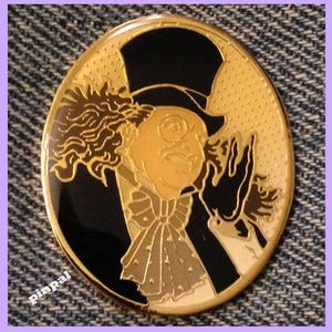 May include: A gold-colored metal pin featuring a cartoon image of the Penguin from Batman. The Penguin is wearing a black top hat, a black tuxedo, and a white bow tie. He has a white face with black eyes and a black mustache. The background is a black circle with a gold-colored dotted pattern.