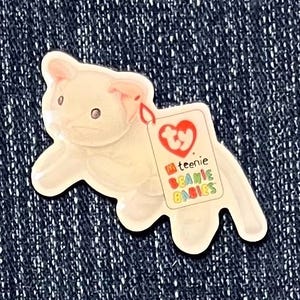 May include: White plush toy pig with a Ty Beanie Babies tag attached. The tag is red, yellow, green, and blue with the words "Ty" and "teenie beanie babies".