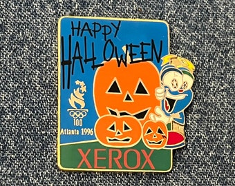 May include: A gold pin with a blue, white, and red cartoon character holding a pumpkin. The pin says "Happy Halloween" and "Xerox" with the 1996 Atlanta Olympics logo.