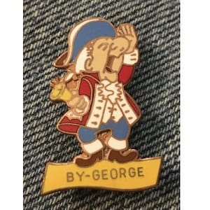 Puede incluir: Un pin de color dorado con una imagen de dibujos animados de un hombre que lleva un sombrero azul, una chaqueta roja y pantalones blancos. El hombre sostiene una campana dorada y el pin dice "BY-GEORGE" en una pancarta amarilla.
