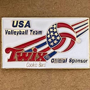 May include: Rectangular pin featuring the USA Volleyball Team logo. The design includes a volleyball with the American flag, the Twix logo, and the words "Official Sponsor."