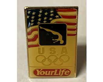 May include: Gold-colored pin with an image of a gymnast performing a back handspring, the American flag, and the Olympic rings. The text "USA" and "YourLife" are also on the pin.