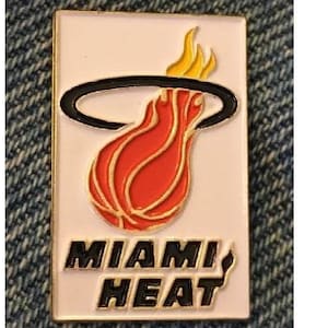 May include: A rectangular pin featuring the Miami Heat logo. The logo includes a stylized basketball on fire, with a black ring around the flames. The words "MIAMI HEAT" are printed in black letters on the bottom.