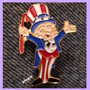 Puede incluir: Un pin de color dorado de Uncle Sam con un sombrero y un traje rojo, blanco y azul. Lleva una caña de caramelo roja y blanca en la mano izquierda y saluda con la mano derecha.