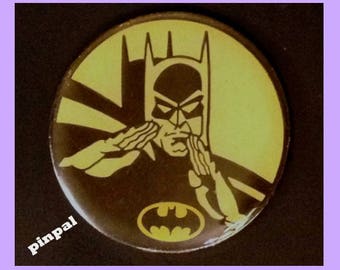 May include: A yellow and brown round pinback button featuring a black and white illustration of Batman with his cape in the background. The Batman logo is in the lower center of the button.