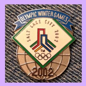 Può includere: Uno spillo d'argento e blu con il testo "Olympic Winter Games Salt Lake City 2002" e una grafica stilizzata di cinque edifici. Lo spillo presenta anche gli anelli olimpici e il testo "2002" in un carattere più grande.