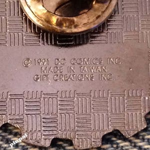 May include: Close-up of the back of a pin featuring the text "&copy; 1991 DC COMICS INC. MADE IN TAIWAN GIFT CREATIONS INC."