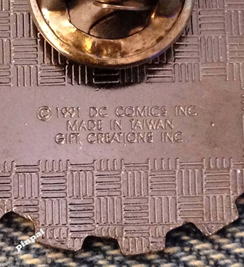May include: Close-up of the back of a pin featuring the text "&copy; 1991 DC COMICS INC. MADE IN TAIWAN GIFT CREATIONS INC."