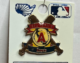 May include: Collector's pin featuring the Los Angeles Angels baseball team logo. The pin has a gold-colored design with the team's "A" logo in red, set against a yellow background, and crossed bats. The pin is on a white card.