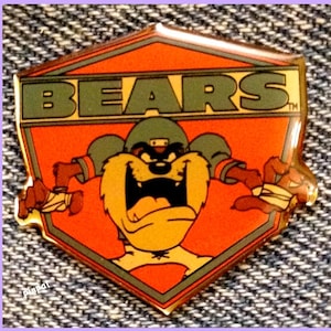 May include: A red, green, and yellow enamel pin featuring a cartoon Tasmanian Devil wearing a football uniform and the word "BEARS" in green letters.