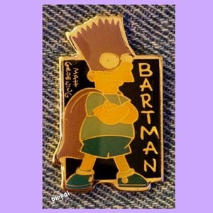 May include: A Bartman pin featuring Bart Simpson in a superhero pose. The pin has a black background with the word "BARTMAN" in yellow. Bart is wearing a green shirt and shorts, with a brown cape. The pin also includes the text "Matt Groening".