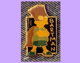 May include: A Bartman pin featuring Bart Simpson in a superhero pose. The pin has a black background with the word "BARTMAN" in yellow. Bart is wearing a green shirt and shorts, with a brown cape. The pin also includes the text "Matt Groening".