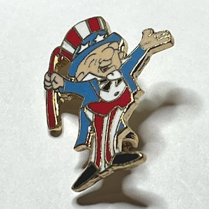 Puede incluir: Un pin dorado del Tío Sam. El pin presenta al Tío Sam con un abrigo azul, pantalones a rayas rojas y blancas y un sombrero a juego. Sostiene un bastón a rayas rojas y blancas. Un accesorio patriótico.