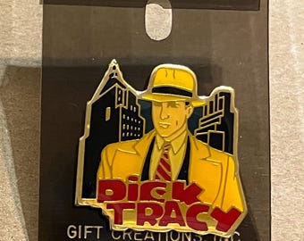 May include: A Dick Tracy pin featuring the character in a yellow suit and hat, red tie, and the words "Dick Tracy" in red. The pin is set against a cityscape backdrop and is on a black backing.