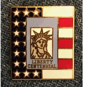 Puede incluir: Un pin de color dorado con un diseño de bandera americana azul, blanca y roja. El centro del pin presenta una representación de la Estatua de la Libertad con el texto "LIBERTY CENTENNIAL".